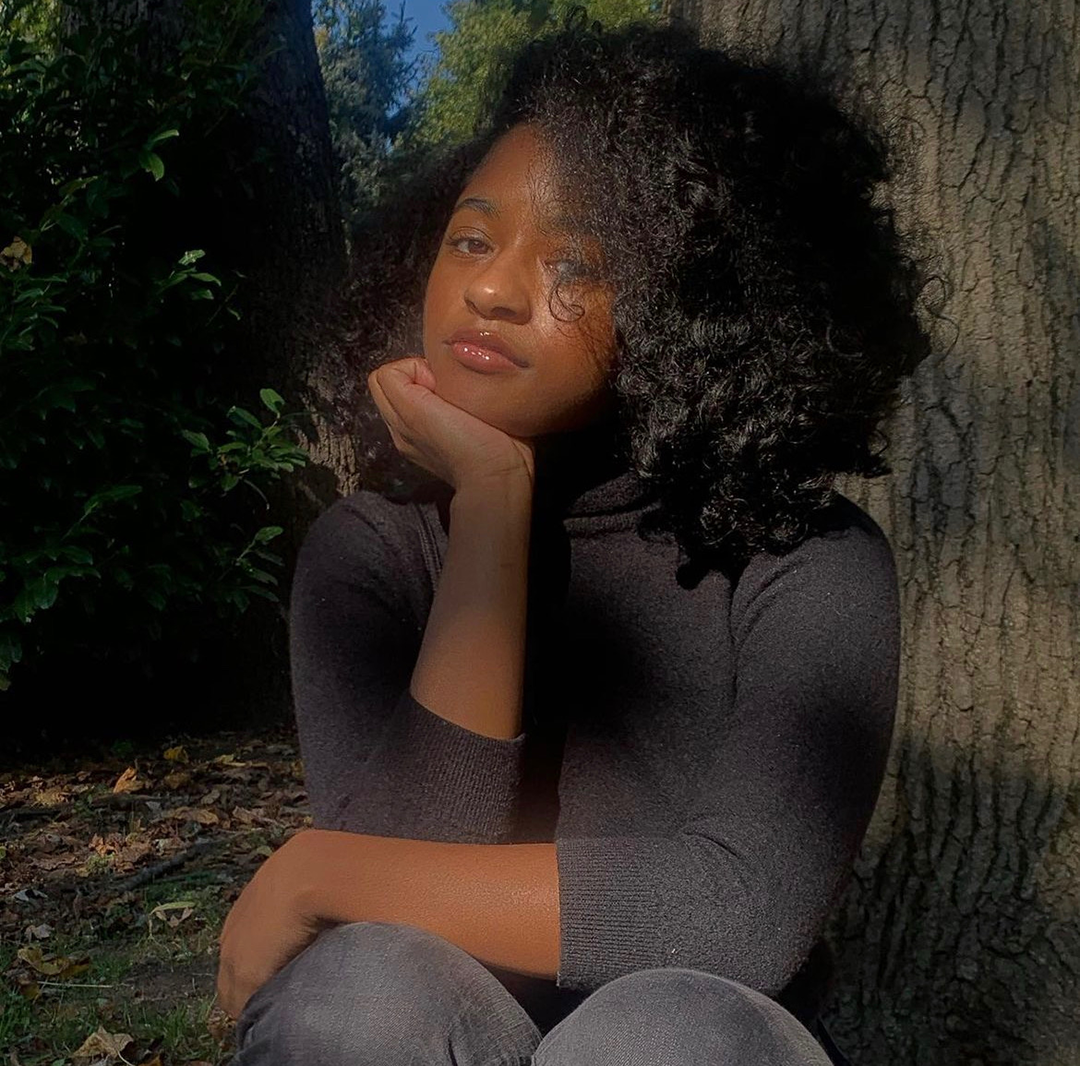 Student Alexis Robinson sitting with head propped in hand by a tree
